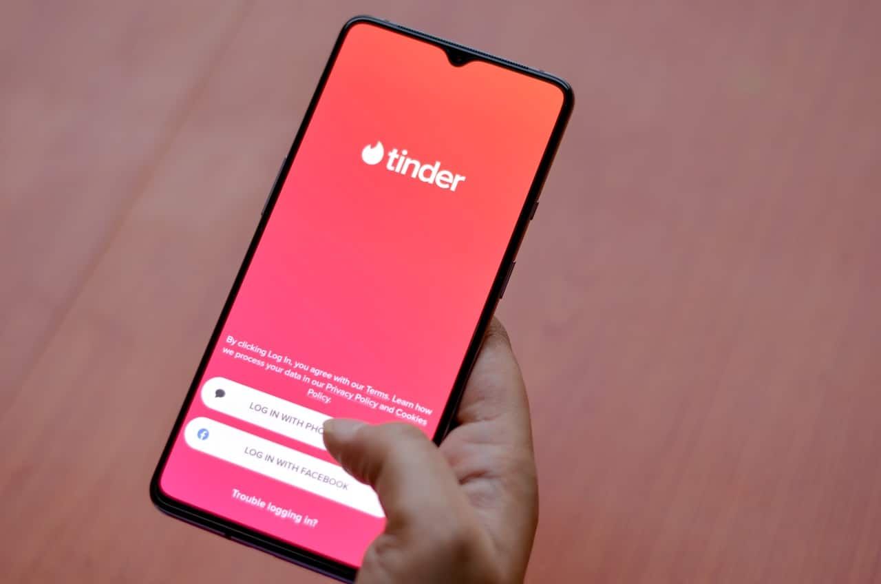 Flat lay with wooden background and Tinder app logo on display on a smartphone screen in female hands.