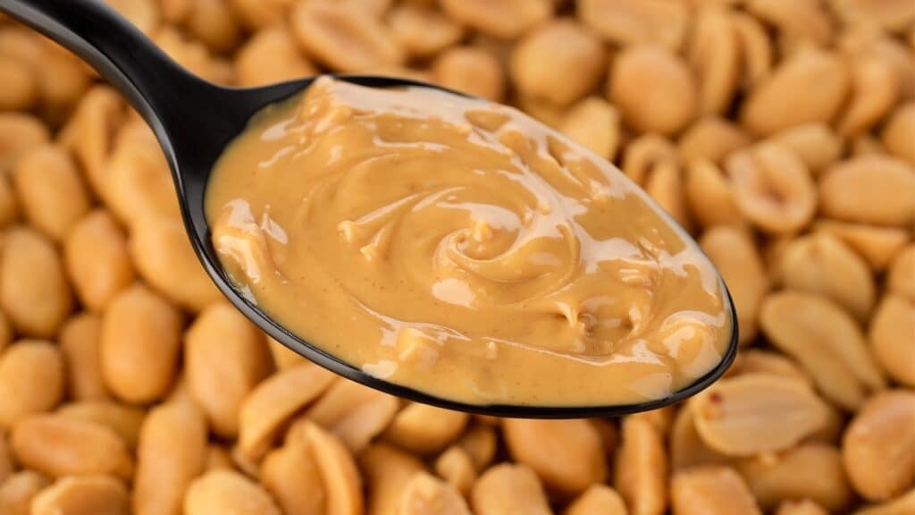Peanut butter in spoon and peanuts on background