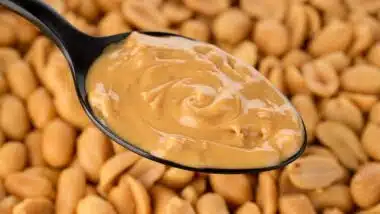 Peanut butter in spoon and peanuts on background