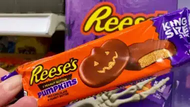 A hand holding king size Reese's peanut butter pumpkins inside a store.