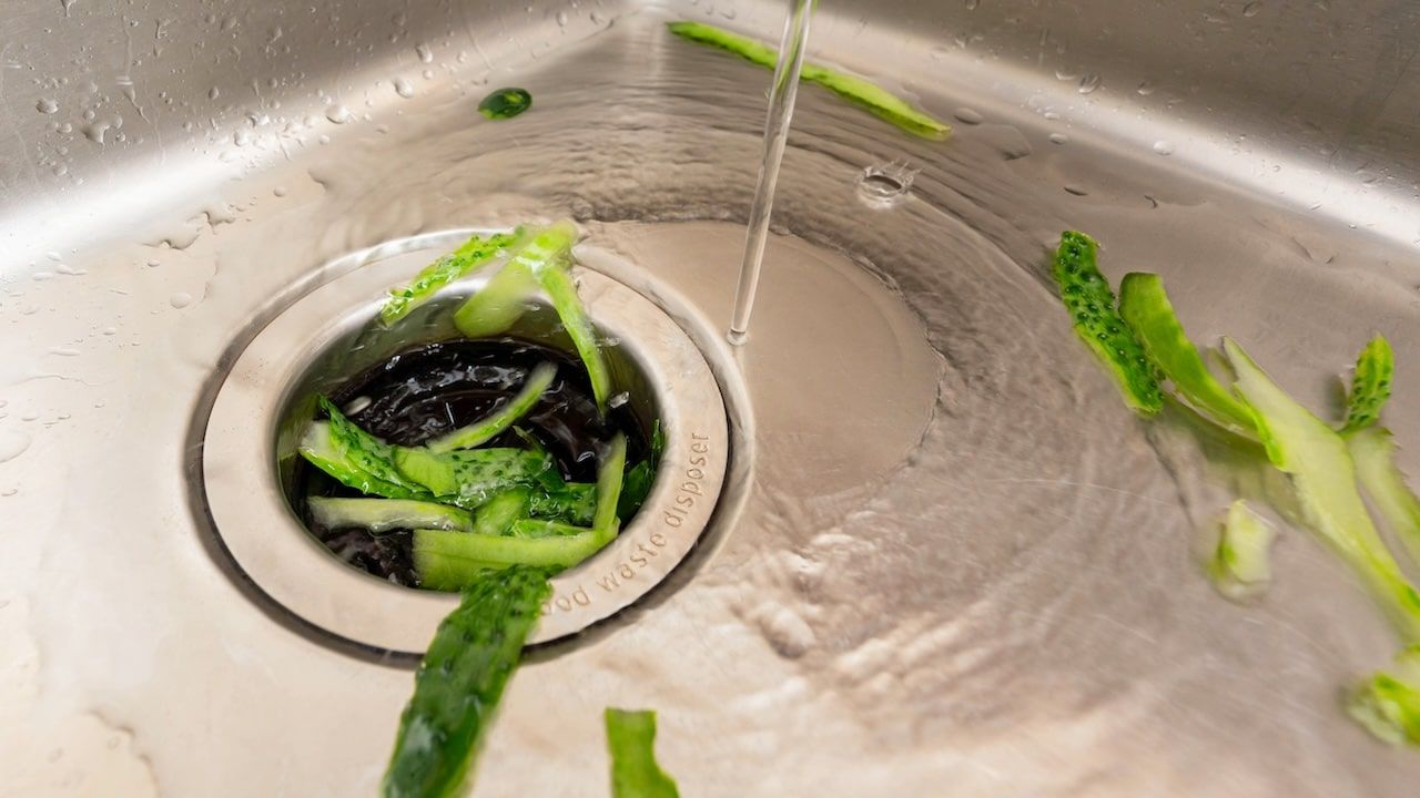 kitchen waste disposal system handling cucumber peels with running water in a modern sink setup.