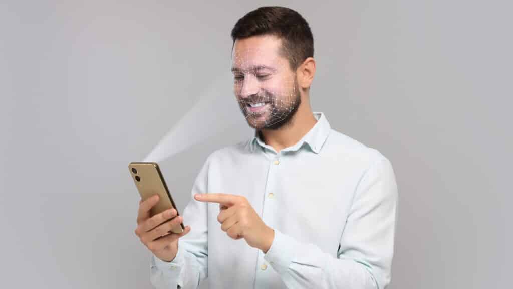 Man unlocking his smartphone with facial recognition app against light grey background.