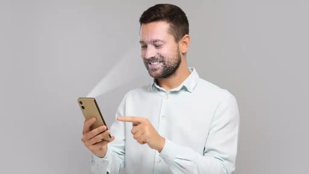 Man unlocking his smartphone with facial recognition app against light grey background.