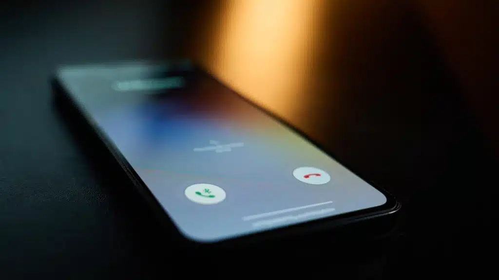Close-up of smartphone lying on table in dark room with incoming call on screen.