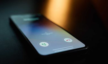 Close-up of smartphone lying on table in dark room with incoming call on screen.