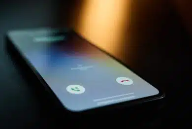 Close-up of smartphone lying on table in dark room with incoming call on screen.