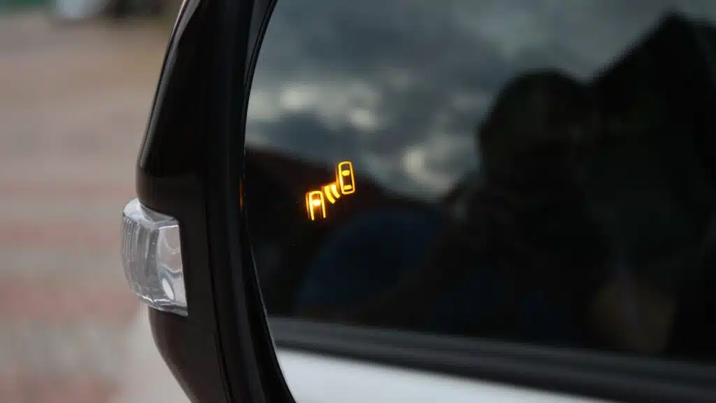 Car side mirror with illuminated orange blind spot monitoring warning indicator