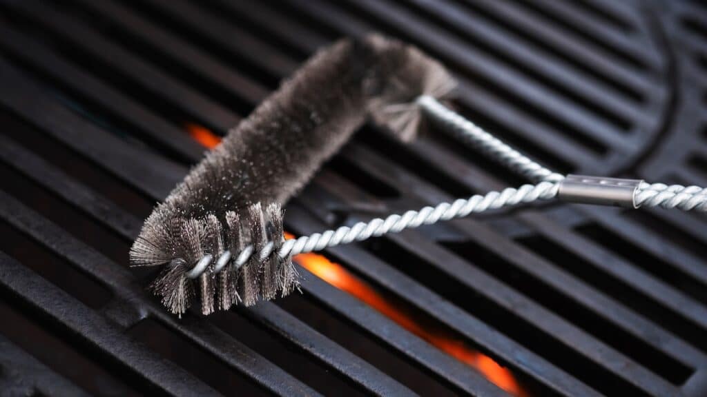 Cleaning outdoor gas grill with a metal brush before next grilling.