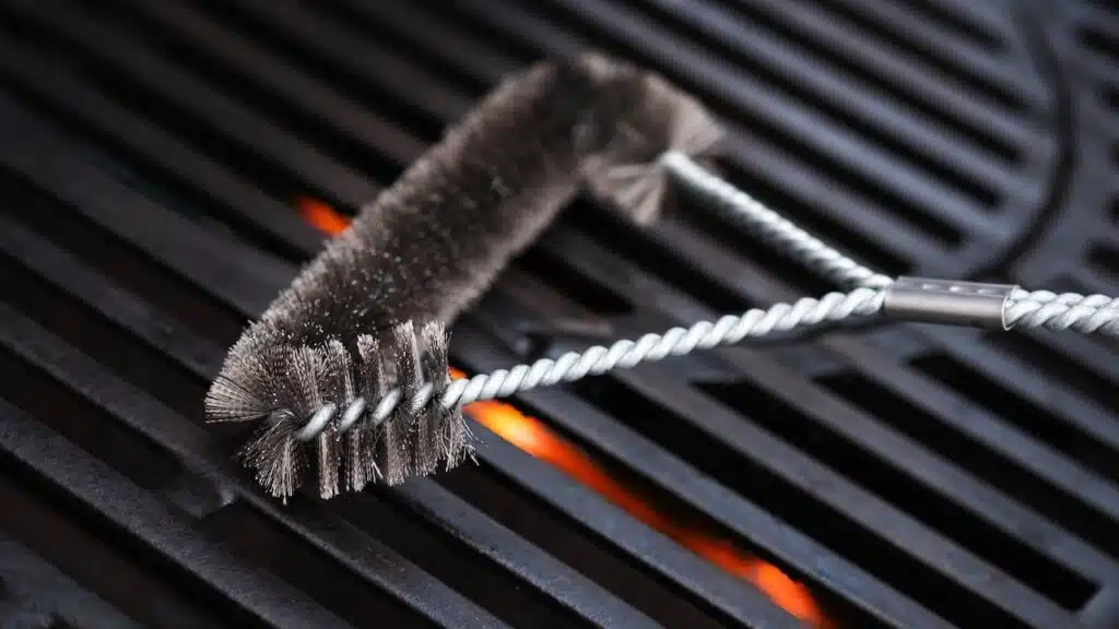 Cleaning outdoor gas grill with a metal brush before next grilling.