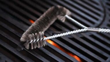 Cleaning outdoor gas grill with a metal brush before next grilling.