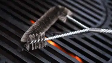 Cleaning outdoor gas grill with a metal brush before next grilling.