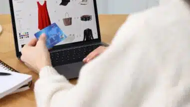 Woman with laptop and credit card shopping online at wooden table in kitchen, closeup