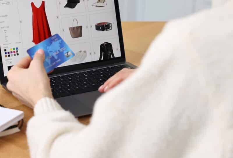 Woman with laptop and credit card shopping online at wooden table in kitchen, closeup