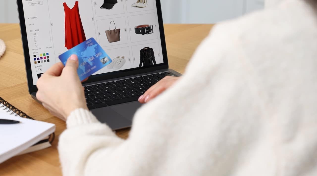 Woman with laptop and credit card shopping online at wooden table in kitchen, closeup