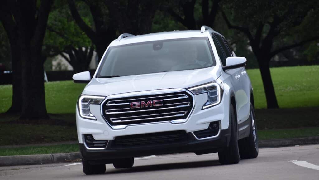A portrait of a white GMC mid-sized SUV cruising at a nature reserve.