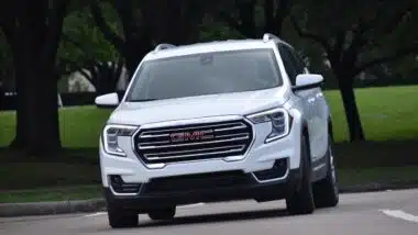 A portrait of a white GMC mid-sized SUV cruising at a nature reserve.