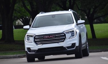 A portrait of a white GMC mid-sized SUV cruising at a nature reserve.