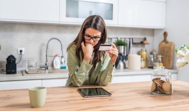 holding a credit card and staring at a tablet concerned about fraud, hidden fees, and tight budgeting while shopping from home