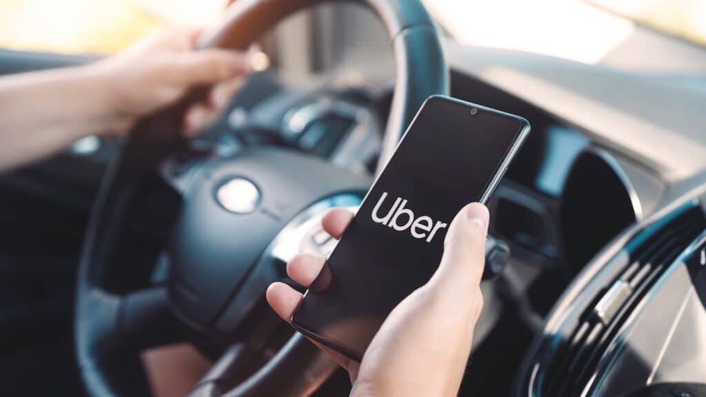 Uber driver holding smartphone in car.