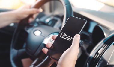 Uber driver holding smartphone in car.