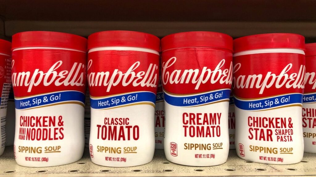 shelf with containers of Campbell's Chicken Noodle, Chicken Stars, Classic and Creamy tomato Soups in convenient to go cups. Microwavable