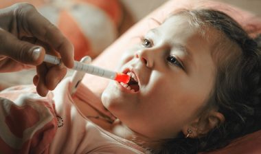 Father giving medicine to sick child with syringe.