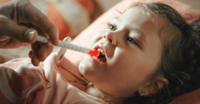 Father giving medicine to sick child with syringe.