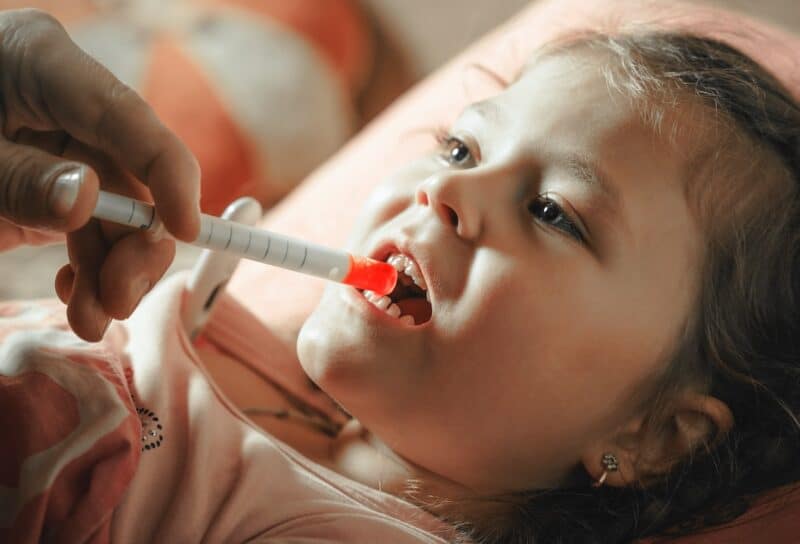 Father giving medicine to sick child with syringe.
