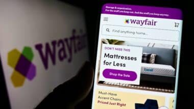 Person holding cellphone with website of US e-commerce company Wayfair Inc. on screen in front of logo.