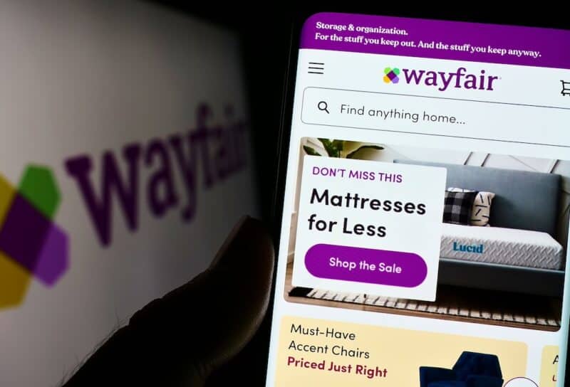 Person holding cellphone with website of US e-commerce company Wayfair Inc. on screen in front of logo.