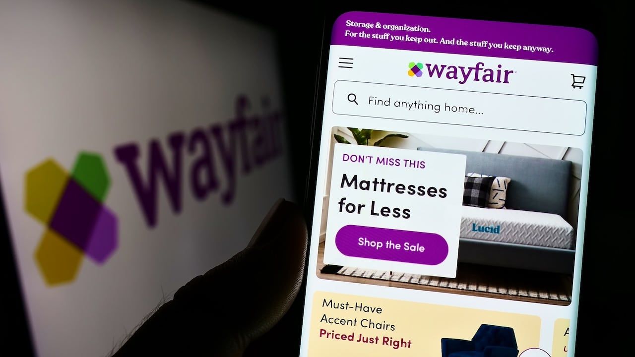 Person holding cellphone with website of US e-commerce company Wayfair Inc. on screen in front of logo.