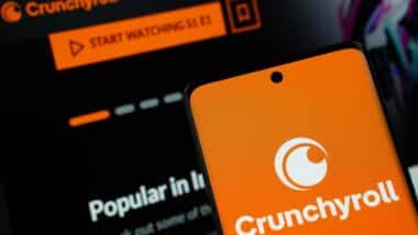 Crunchyroll logo is displayed on a smartphone screen, with the crunchyroll website visible on a computer screen in the background.
