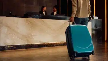 Close up of hotel guest with a suitcase arriving reception desk.