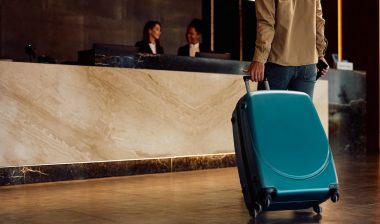 Close up of hotel guest with a suitcase arriving reception desk.