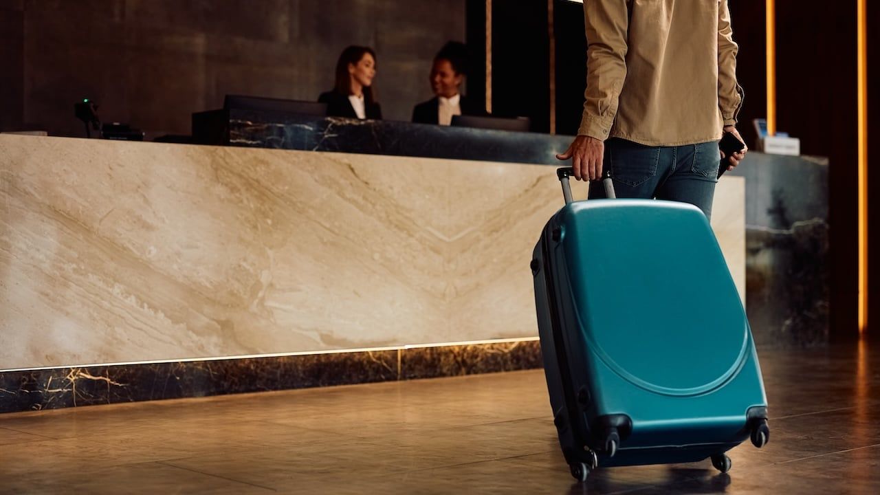 Close up of hotel guest with a suitcase arriving reception desk.