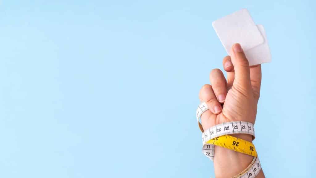 Slim patches with measuring tape and woman hand on blue background