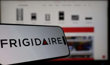 Smartphone displaying Frigidaire logo in front of the company website on a monitor