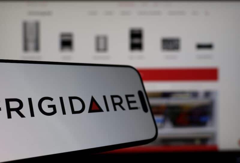 Smartphone displaying Frigidaire logo in front of the company website on a monitor