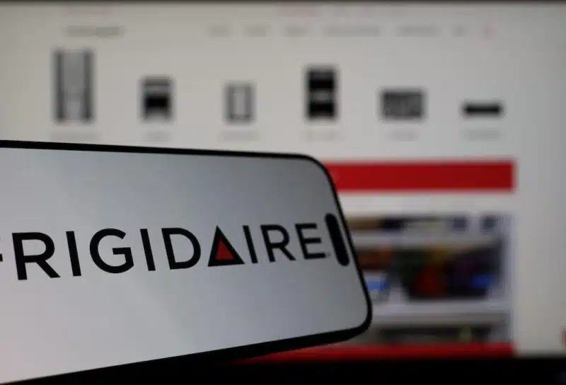 Smartphone displaying Frigidaire logo in front of the company website on a monitor