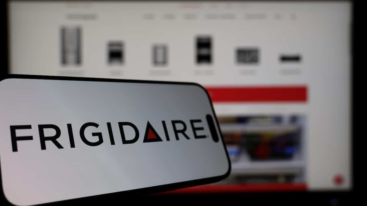 Smartphone displaying Frigidaire logo in front of the company website on a monitor