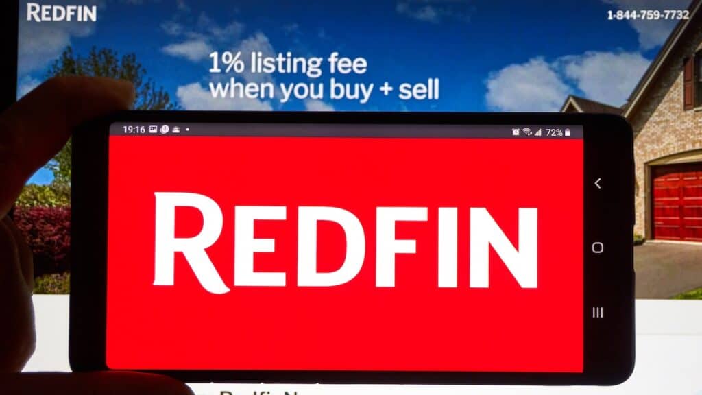 Redfin logo on a cell phone over an official site. Redfin is a real estate brokerage, it is Seattle-based company was founded in 2004.
