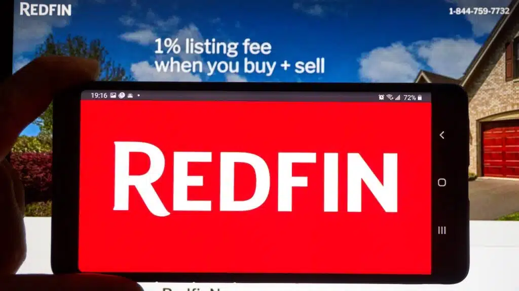Redfin logo on a cell phone over an official site. Redfin is a real estate brokerage, it is Seattle-based company was founded in 2004.
