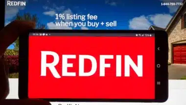 Redfin logo on a cell phone over an official site. Redfin is a real estate brokerage, it is Seattle-based company was founded in 2004.