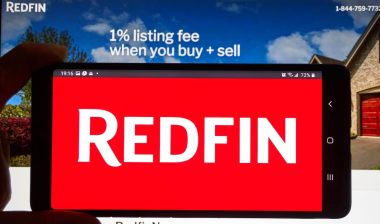 Redfin logo on a cell phone over an official site. Redfin is a real estate brokerage, it is Seattle-based company was founded in 2004.
