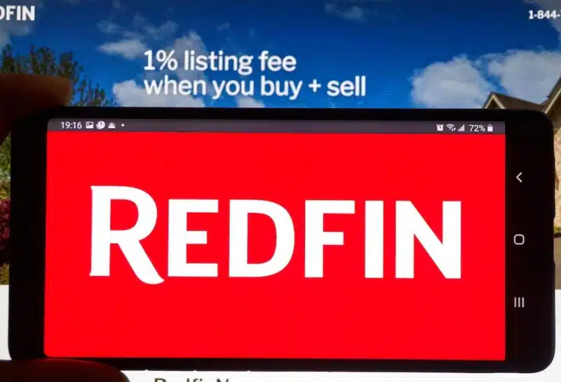 Redfin logo on a cell phone over an official site. Redfin is a real estate brokerage, it is Seattle-based company was founded in 2004.
