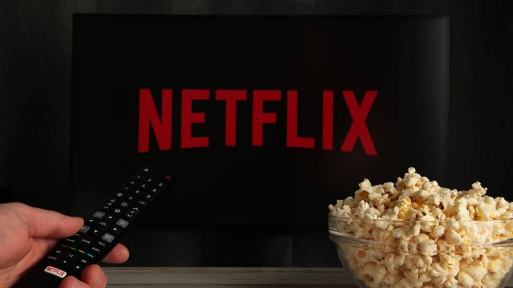 Man with TV remote control in hand and Netflix logo in background.