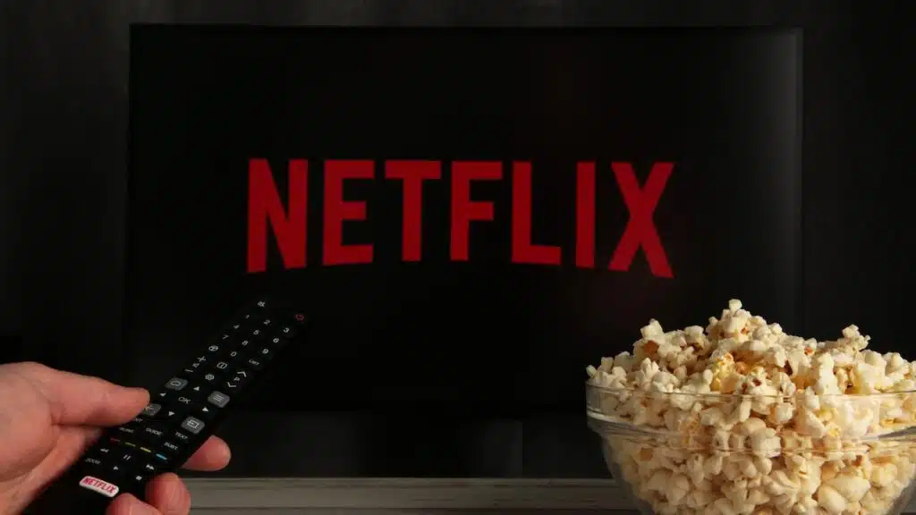 Man with TV remote control in hand and Netflix logo in background.
