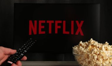 Man with TV remote control in hand and Netflix logo in background.