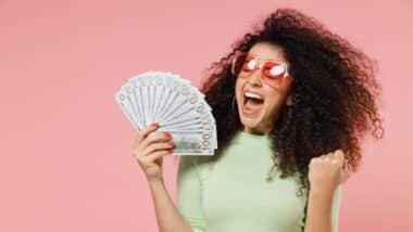 Exultant happy woman 20s hold fan of cash money in dollar banknotes