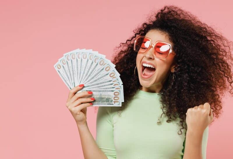 Exultant happy woman 20s hold fan of cash money in dollar banknotes